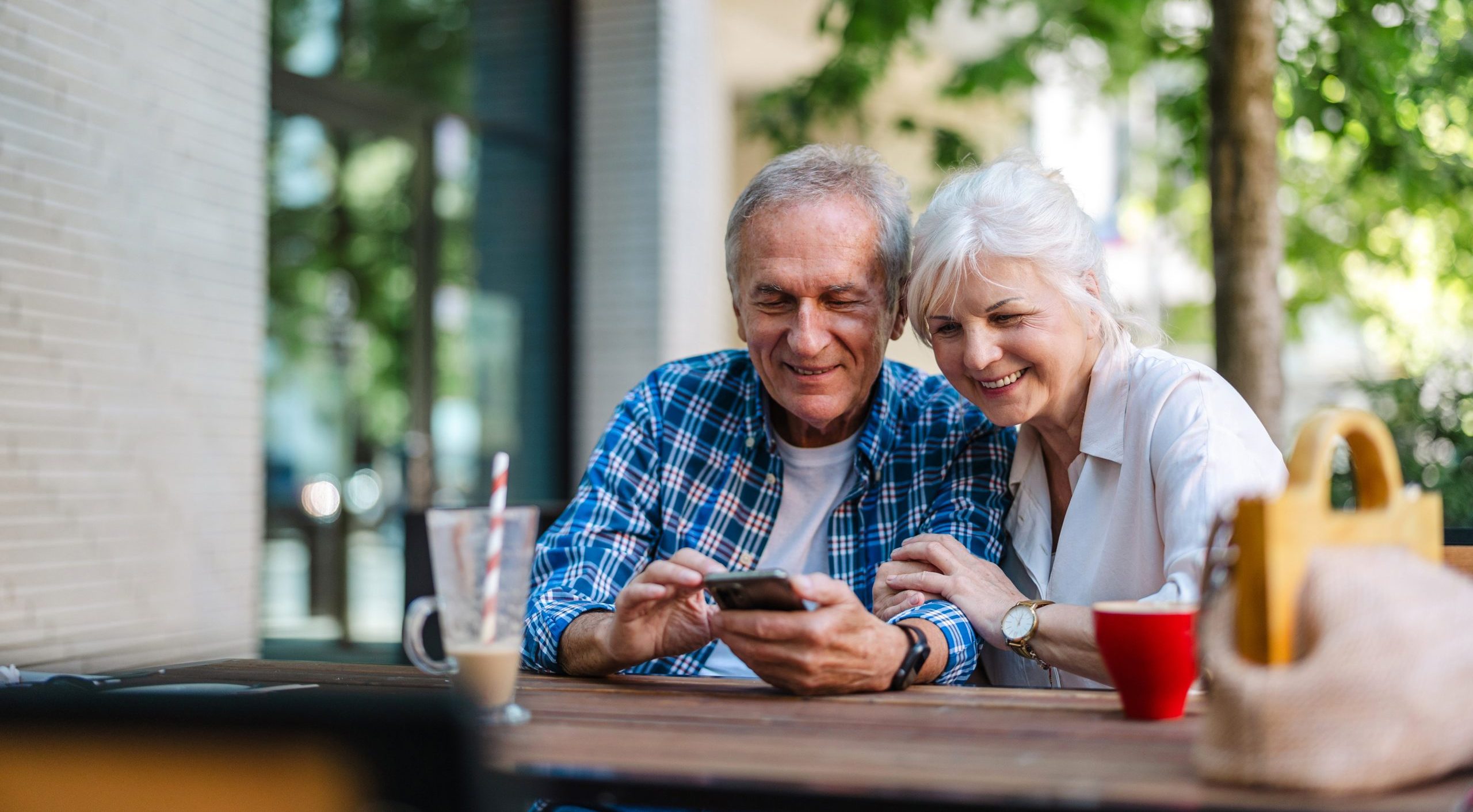 Retired Senior couple sitting at a table in a cafe and using mobile phone mid-year retirement checkup