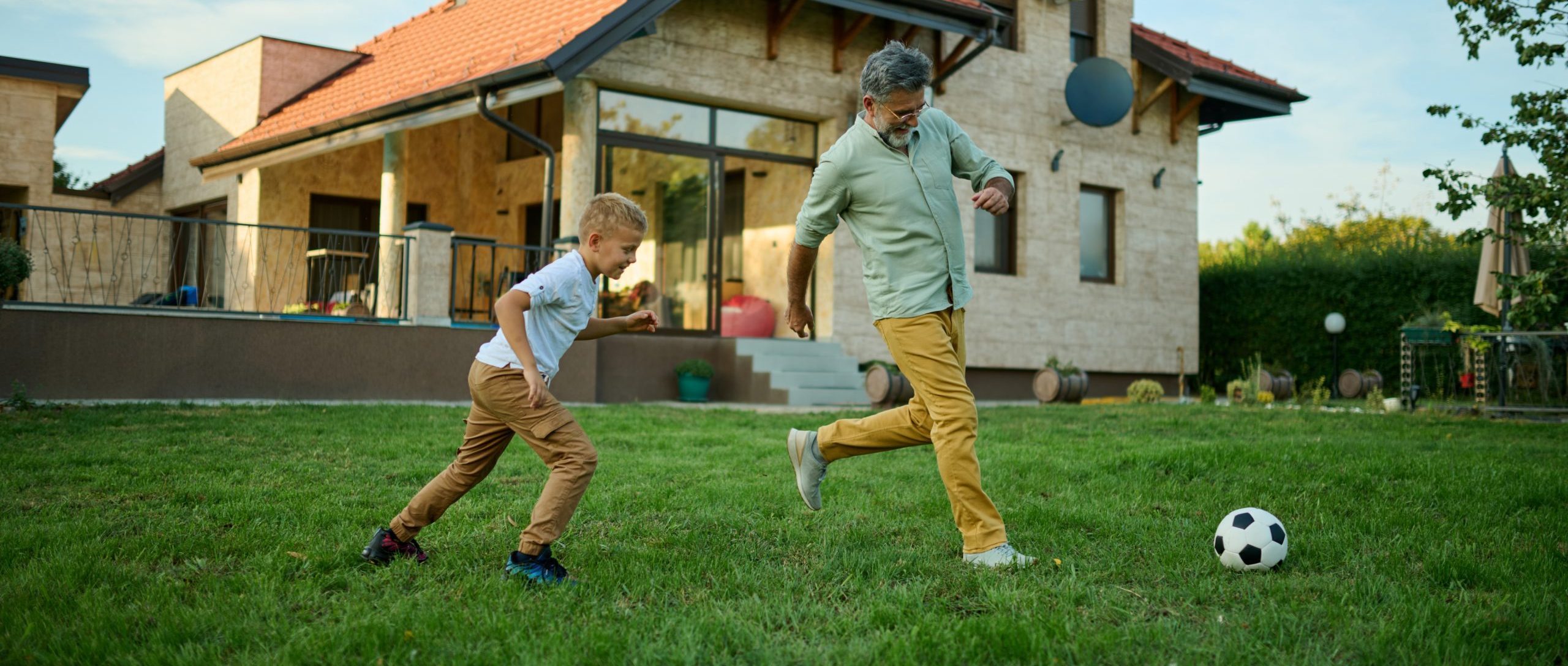 Grandfather and grandson play soccer in backyard, bonding over game and creating joyful memories