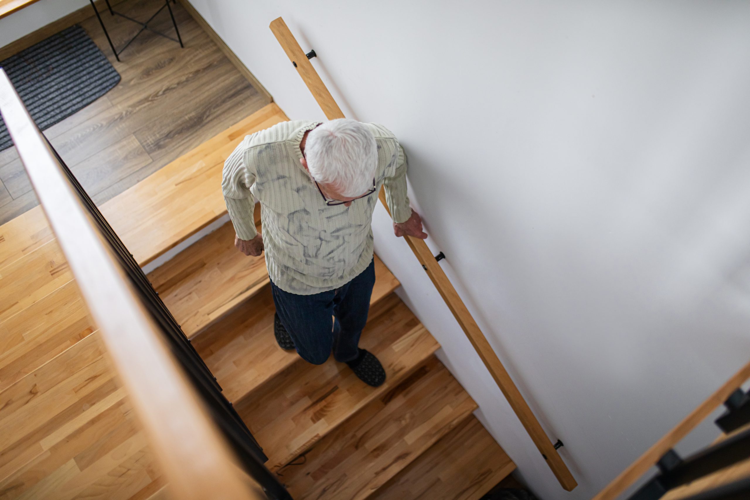 Senior adult navigating his home staircase with the support of a handrail, highlighting practical home safety adaptations that help older adults age in place