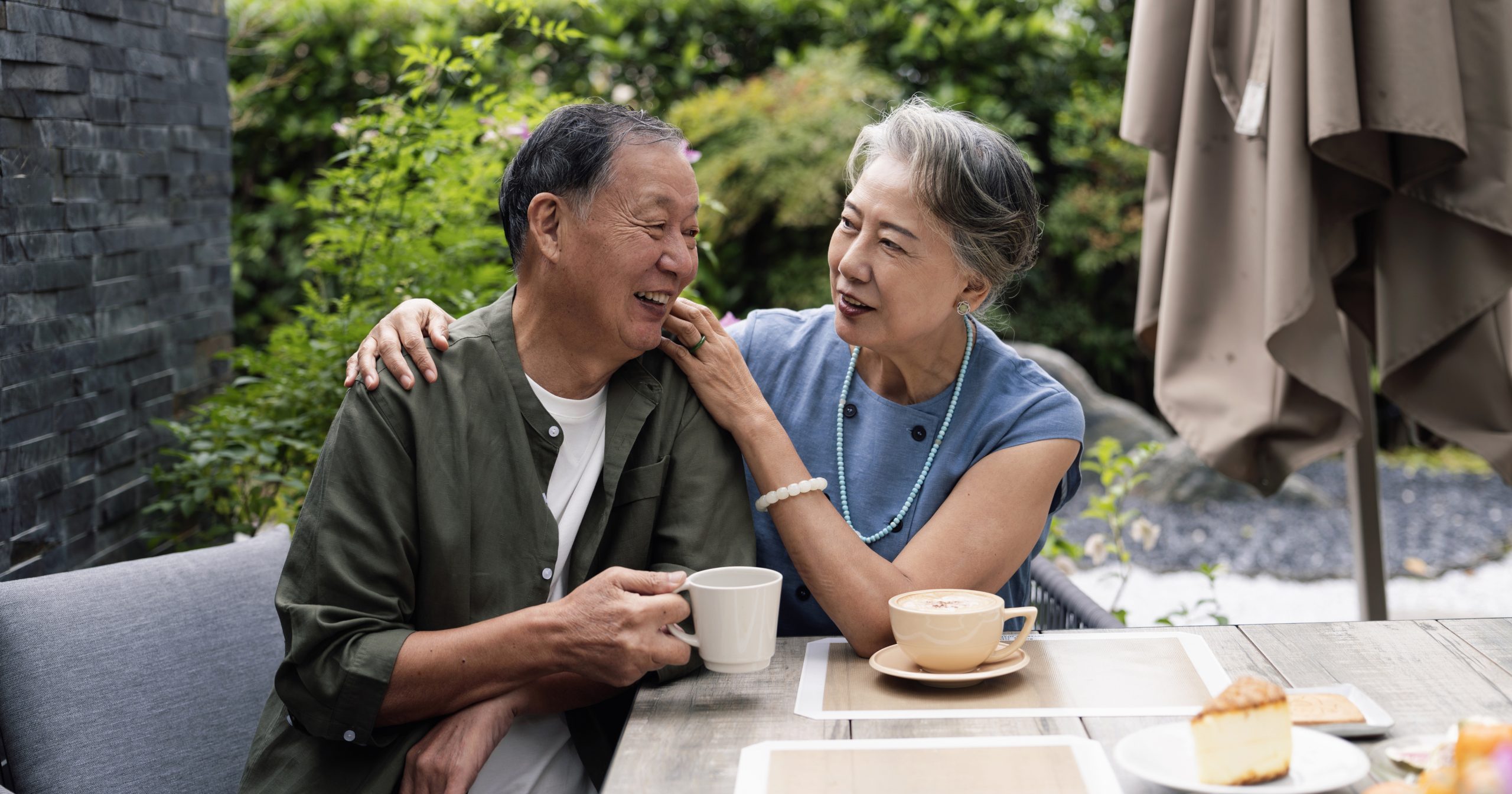 Senior heterosexual couple relaxing together at the picnic table in the yard outdoors by eating dessert and drinking tea on sunny day.They are enjoying weekend together.
